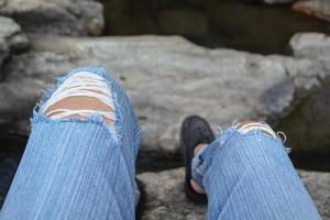 alguien se sienta en la roca usando jeans rotos de cerca. foto