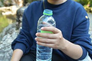 alguien con suéter azul sosteniendo una botella de agua de plástico verde. foto