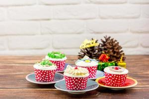Christmas bakery concept. Cupcake with buttercream and topping, Santa Claus, Rudolf, and a Christmas tree on a wooden table. photo
