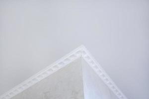 Detail of corner ceiling with intricate crown molding. Suspended ceiling and drywall construction in empty room in apartment or house. Stretch ceiling white and complex shape. photo