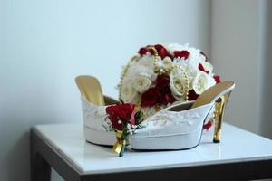 A pair of white women's high heels and a beautiful rose flower bucket. photo