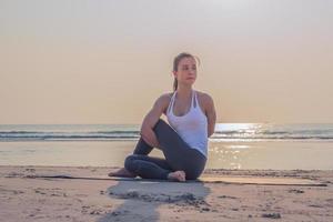 joven asiática sana haciendo ejercicio de yoga en la playa por la mañana. foto