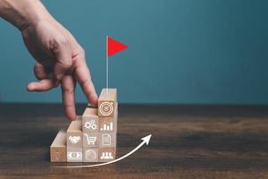 Step by step to grow your business, business success or career path success concept. Man use finger walking up to the top target with red flag on wooden blocks arranged in a shape of staircase. photo