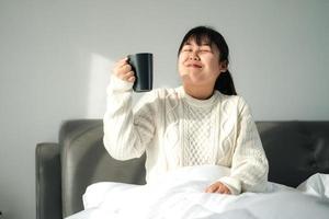 mujer joven bebiendo café en el dormitorio, mujer sosteniendo una taza de café en la cama. foto