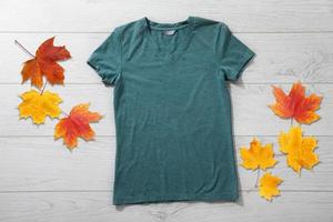 maqueta de camisa verde - camiseta con hojas de otoño en un escritorio de madera blanca foto