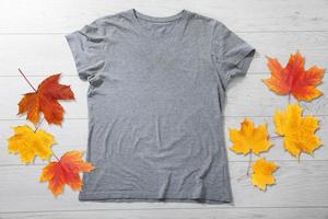 maqueta de camisa gris - camiseta con hojas de otoño en un escritorio de madera blanca foto