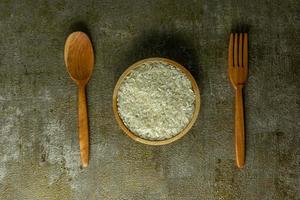 uncooked rice or dry rice. raw rice in wooden bowl with wooden spoon and fork photo