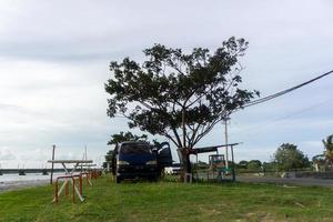 concepto de cafetería móvil. silla y mesa frente a la autocaravana. concepto de picnic. autocaravana estacionada debajo del árbol y al lado del río. foto