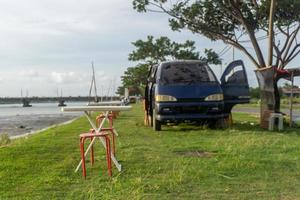 silla y mesa frente a la autocaravana. concepto de picnic. autocaravana estacionada debajo del árbol y al lado del río. concepto de cafetería móvil foto