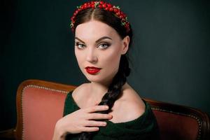 portrait of smiling young beautiful brunette with red wreath and braid on dark background photo