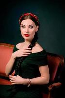 portrait of smiling young beautiful brunette with red wreath and braid on dark background photo