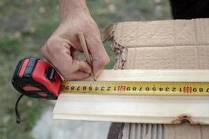 las manos del carpintero miden con una cinta métrica en una tabla de madera y marcan la longitud requerida con un lápiz. foto