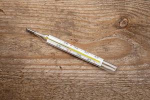 Medical mercury thermometer with a temperature of 37 degrees on a wooden texture. Top view. photo