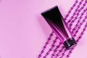 Luxurious black and pink squeeze cosmetic bottles and purple decorations on pastel background. photo