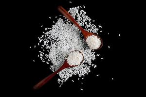 White uncooked rice in wooden spoons on black background. Raw grains of long rice. photo