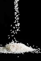 Raw white rice is falling on table. Pile of uncooked long rice on black background. photo