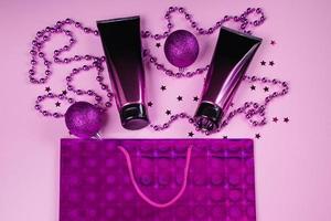 Black and pink cosmetic tubes on pastel background. Squeeze bottles and purple christmas decorations photo