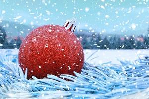 Red shiny Christmas ball on fir branches, with blurred background and falling snow. Christmas, New Year. Copy space photo