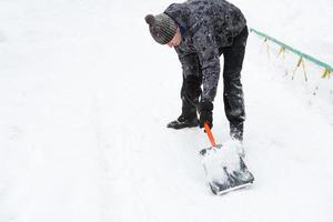 A man cleans snow with a shovel in winter in a swept yard after a snowfall. Winter weather conditions, snow shovel for car trunk photo