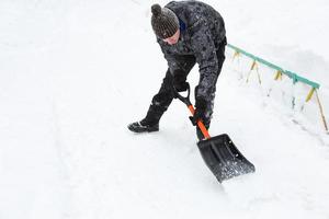 A man cleans snow with a shovel in winter in a swept yard after a snowfall. Winter weather conditions, snow shovel for car trunk