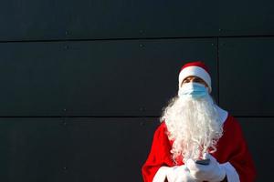 santa claus con barba blanca en abrigo rojo con una máscara médica. navidad en la pandemia del coronavirus, enfermedades estacionales, sars y neumonía en las vacaciones. protección contra virus en el nuevo año foto