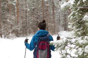 esquiador con mochila y sombrero con pompón con bastones de esquí en las manos sobre el fondo de un bosque nevado. esquí de fondo en bosque de invierno, deportes al aire libre, estilo de vida saludable, turismo de deportes de invierno. foto