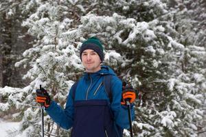 esquiador con mochila y sombrero con pompón con bastones de esquí en las manos sobre el fondo de un bosque nevado. esquí de fondo en bosque de invierno, deportes al aire libre, estilo de vida saludable, turismo de deportes de invierno. foto