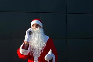 moderno santa claus hablando por teléfono. solicitando los servicios de un animador para navidad y año nuevo. saludos en línea a través de Internet y comunicación móvil, distancia social foto