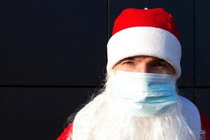 Santa Claus with white beard in red coat in a medical mask. Christmas in the coronavirus pandemic, seasonal diseases, SARS and pneumonia in the holidays. Protection from viruses in the new year photo