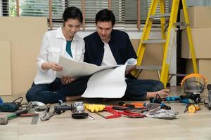 Happy Creative young Asian couple renovating house together and using a blueprint for renovation planning and how to   decorate and arrange the furniture on their new living room space photo