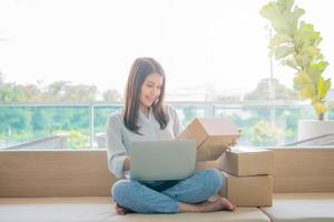 Happy young Asian woman entrepreneur, Smile for sales success after checking order from online shopping store in a laptop at home office, Concept of merchant business online and eCommerce photo