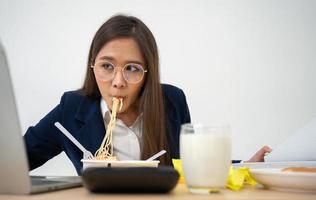 Busy and tired businesswoman eating spaghetti for lunch at the Desk office and working to deliver financial statements to a boss. Overworked and unhealthy for ready meals, burnout concept. photo