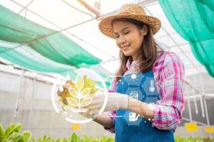 concepto de procesamiento del cultivo del campo agrícola con tecnología digital, tablero digital para monitorear la planta, agricultora sosteniendo una canasta de vegetales frescos en una granja orgánica. foto