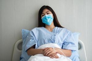 triste mujer paciente asiática acostada en la cama del hospital y usando una máscara para proteger el coronavirus. concepto de atención médica, coronavirus de cuarentena y seguro médico. foto