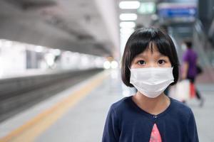 niña pequeña con máscara quirúrgica protección facial gripe y brote de virus en transporte público skytrain o metro. concepto de nuevo estilo de vida normal, utilizando el transporte público para ir a la escuela.