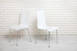 White chairs near the white wall for interior or graphic backgrounds. The chairs can be used to represent interview sessions or waiting rooms for ads purpose. photo