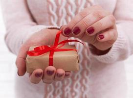 Woman's hands wrapping christmas, holiday handmade present in paper box with red ribbon. Give present box, decoration of gift on vintage wooden table, top view, copy space mock up template for design. photo