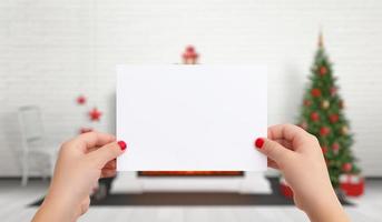 papel en blanco para la tarjeta de felicitación de año nuevo de navidad en manos femeninas. en el fondo hay un árbol de navidad con adornos foto