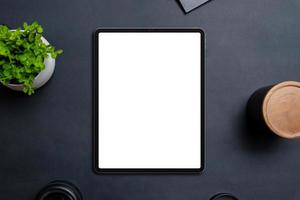 Tablet mockup on black table surrounded by objects. Isolated display in white for app or web design promotion. Top view, flat lay composition photo