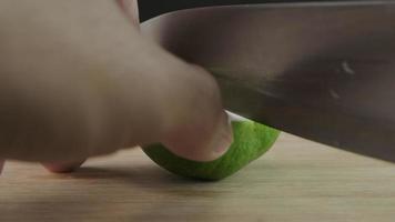 Male hand cutting lemon in half with knife on wooden cutting board in kitchen. Sliced fresh lime fruit with knife close up.