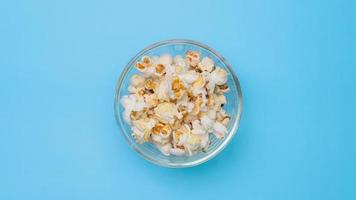 stop motion de délicieux pop-corn dans un bol en verre sur fond bleu pastel. cinéma collation et concept de divertissement. video