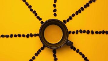 stop motion de café noir dans une tasse avec des grains de café autour sur fond jaune, gros plan.