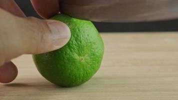 Male hand cutting lemon in half with knife on wooden cutting board in kitchen. Sliced fresh lime fruit with knife close up. video