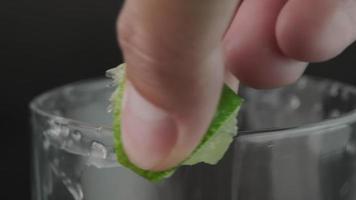 mano exprimiendo cal alrededor del borde del vaso con tequila y sal en primer plano de fondo negro. bebida alcoholica. video