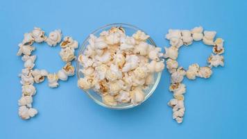 arrêtez le mouvement de délicieux pop-corn dans un bol en verre avec du pop-corn faisant du texte de pop-corn sur fond bleu pastel. cinéma collation et concept de divertissement. video