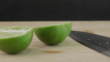 Male hand cutting lemon in half with knife on wooden cutting board in kitchen. Sliced fresh lime fruit with knife close up.