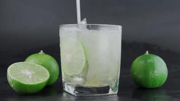 Hand squeezing lime into a glass with ice and lemon slices with limes around on a black background table. alcoholic drink. video