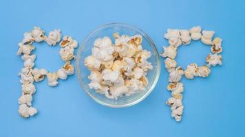 arrêtez le mouvement de délicieux pop-corn dans un bol en verre avec du pop-corn faisant du texte de pop-corn sur fond bleu pastel. cinéma collation et concept de divertissement. video