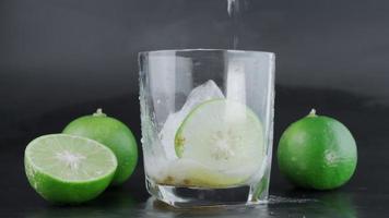 hand- knijpen limoen in een glas met ijs en citroen plakjes met limoenen in de omgeving van Aan een zwart achtergrond tafel. alcoholisch drankje. video