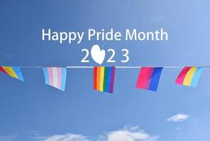 'Happy Pride Month' on bluesky and rainbow flags holding in hand, sunset background, concept for lgbt celebrations in pride month, june, around the world. photo